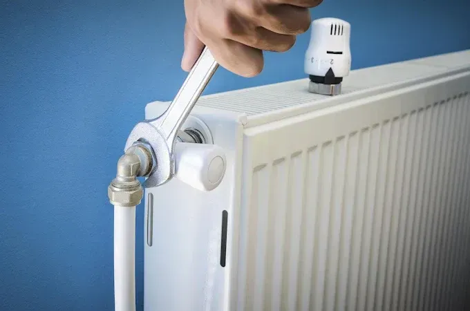 Persona que usa una llave para ajustar la válvula de un radiador blanco contra una pared azul.