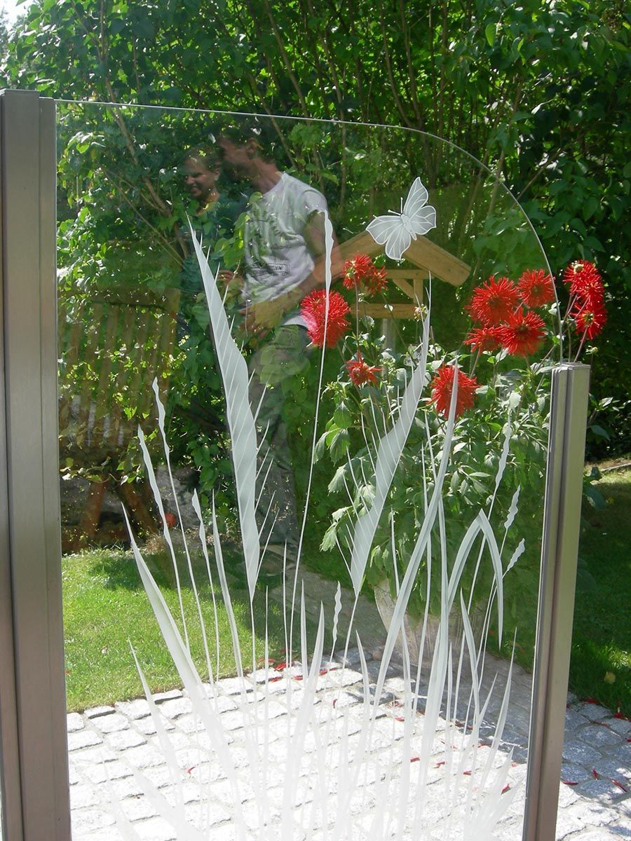 Ein Mann steht in einem Garten hinter einem Glaszaun.