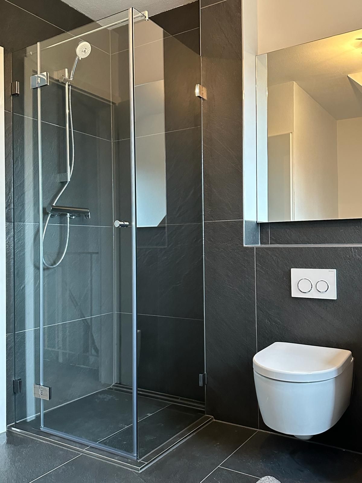 Ein Badezimmer mit ebenerdiger Dusche, mit Glaswand, und Toilette