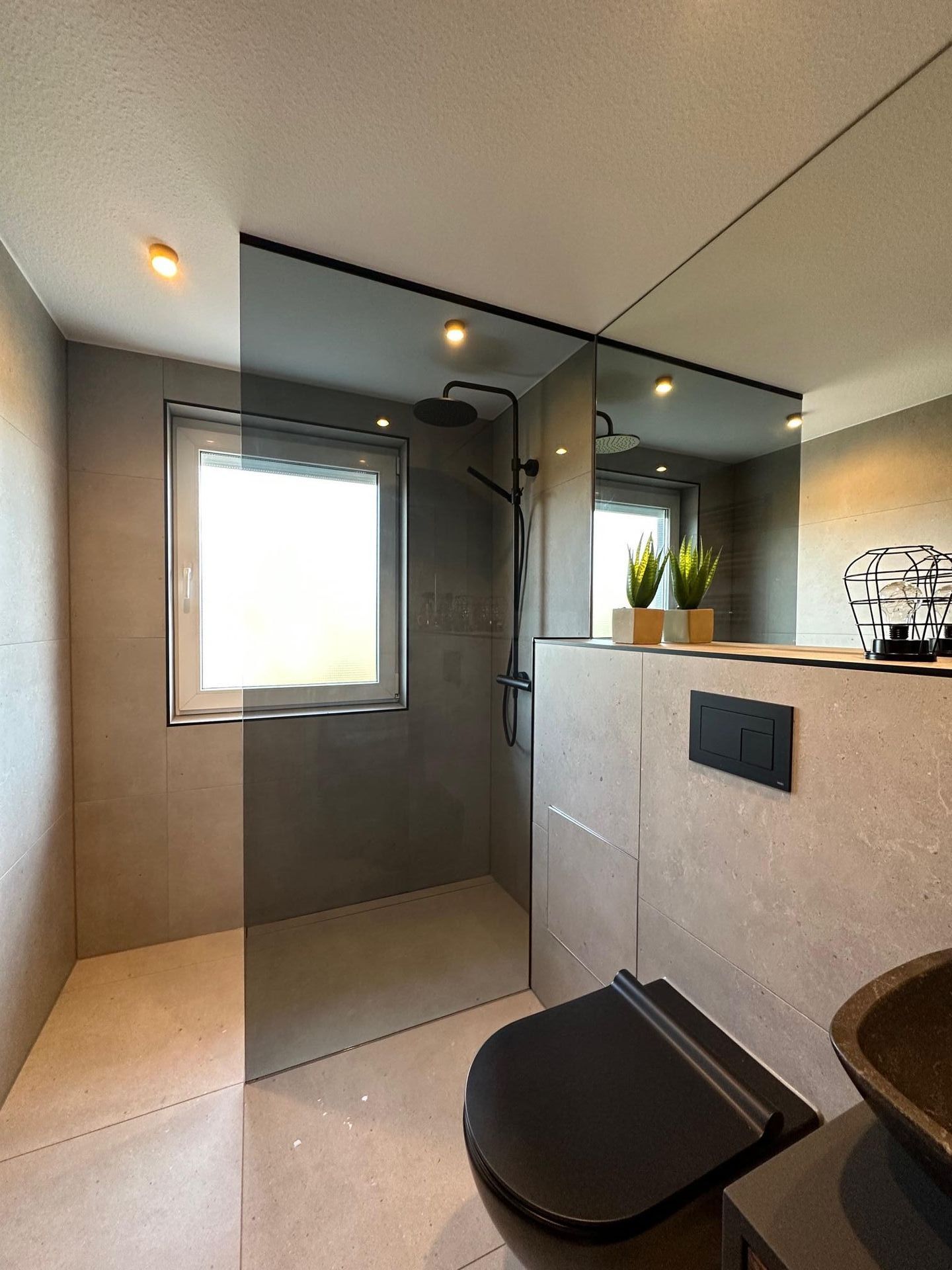 Ein Badezimmer mit ebenerdiger Dusche, mit Glaswand, Toilette, Waschbecken und Spiegel.