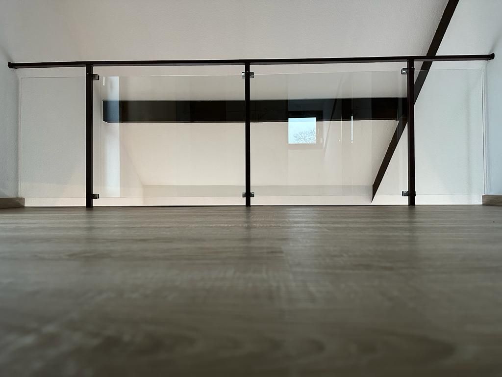 Ein leerer Raum mit einem Glasgeländer und einem Holzboden.