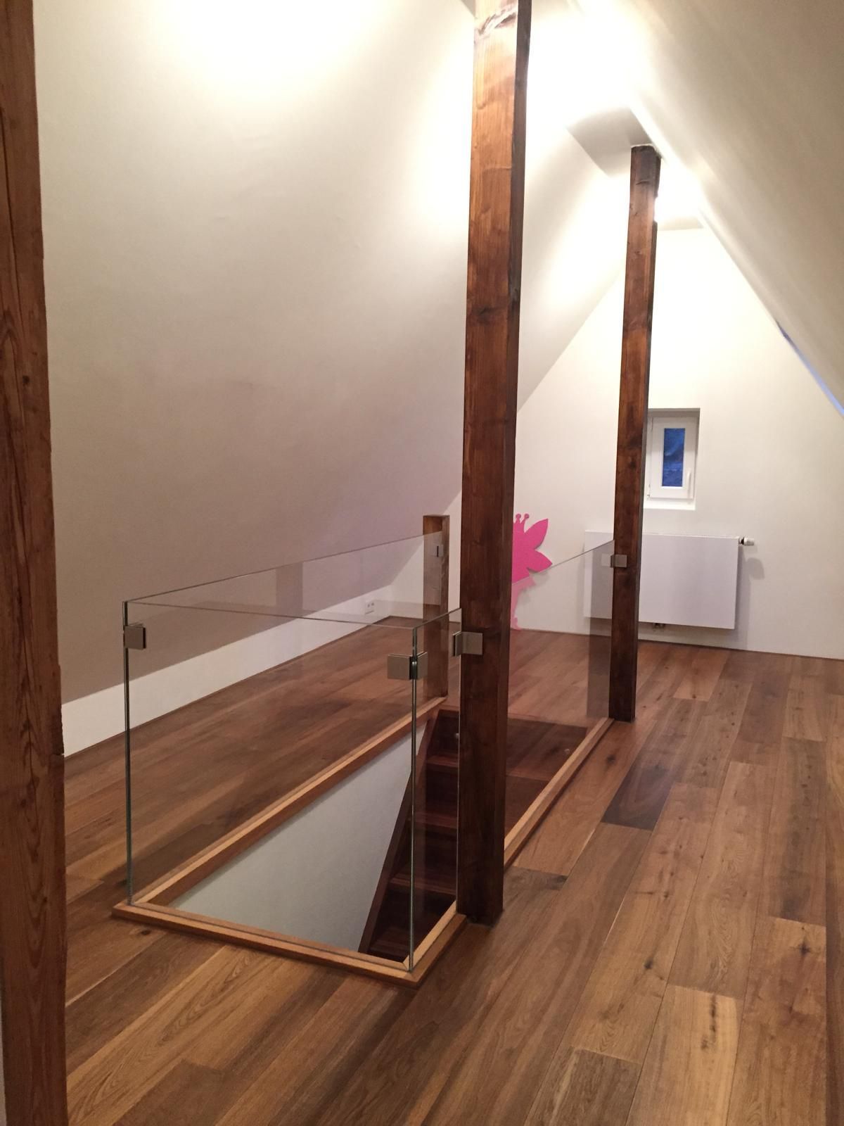Eine Holztreppe mit einem Glasgeländer in einem Dachgeschoss