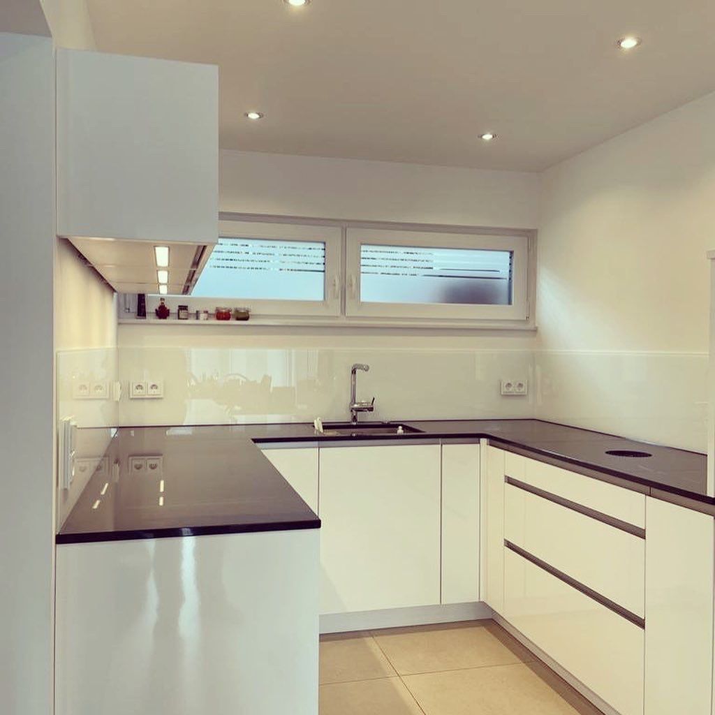 Eine Küche mit weißen Schränken, heller Glasrückwand und schwarzen Arbeitsplatten