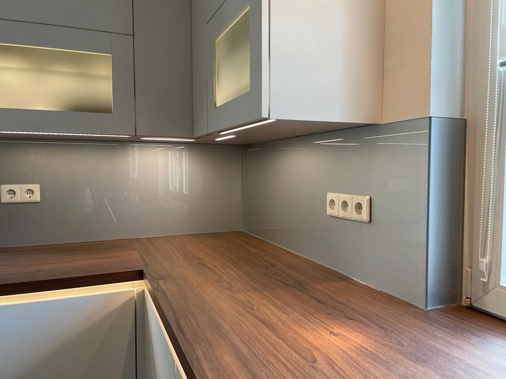 Eine Küche mit Holzarbeitsplatte, Glasrückwänden und grauen Schränken.