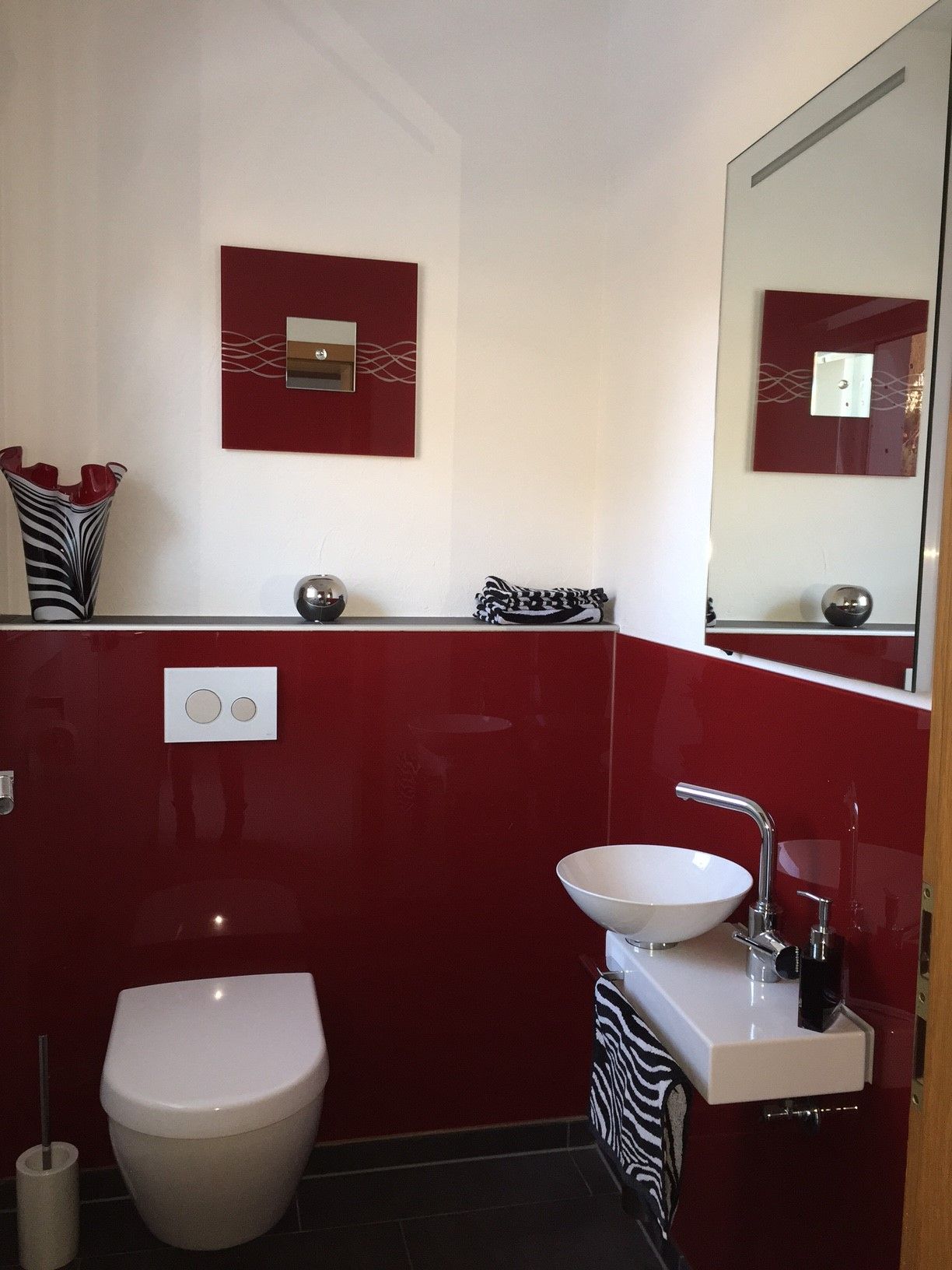 Ein Badezimmer mit Toilette, Waschbecken und Spiegel - rote Glasrückwand 