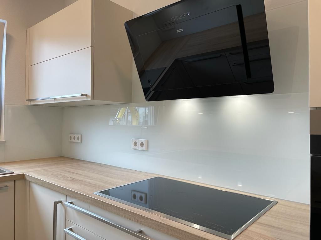 Eine Küche mit weißen Schränken, Glasrückwand und einem schwarzen Herd mit Backofen.