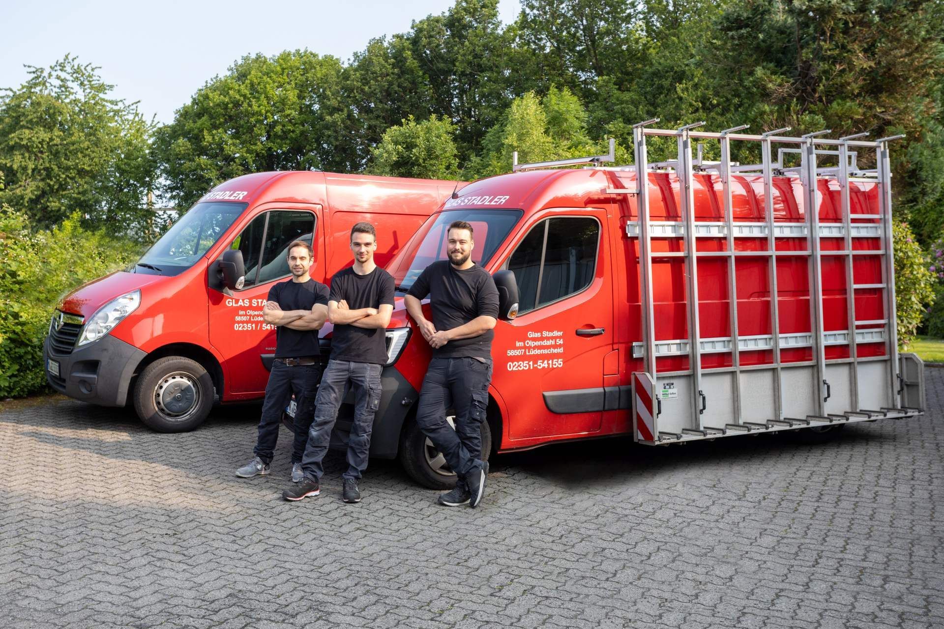 Drei Männer stehen vor zwei roten Lieferwagen.