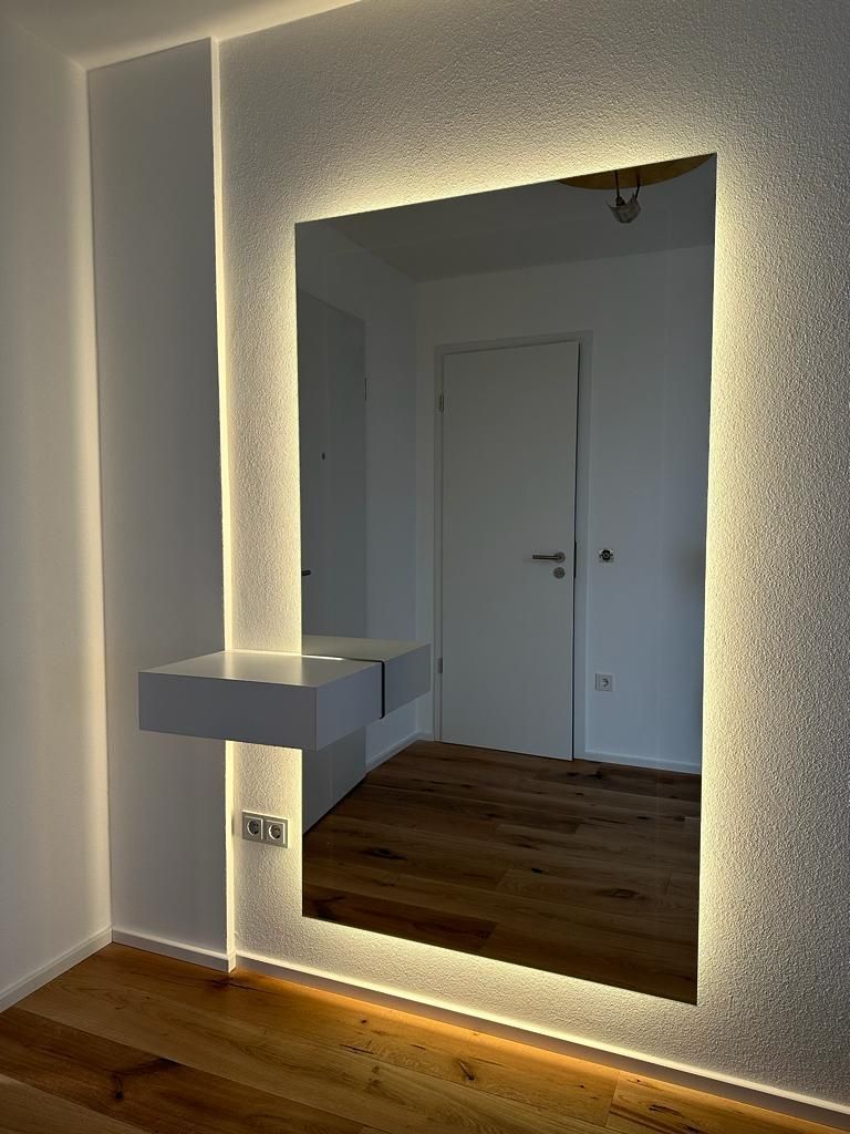 In einem Zimmer hängt ein großer beleuchteter Spiegel an der Wand.