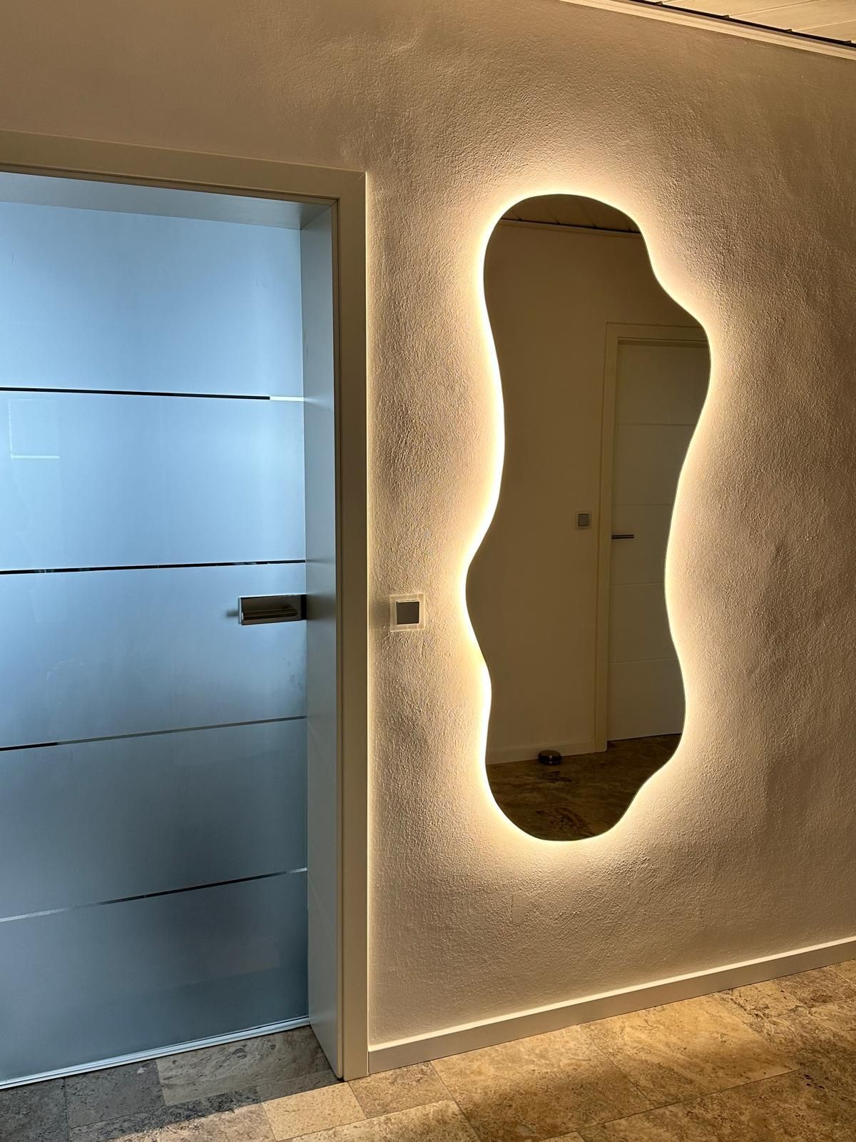 An der Wand neben einer Tür hängt ein großer organischer Spiegel.