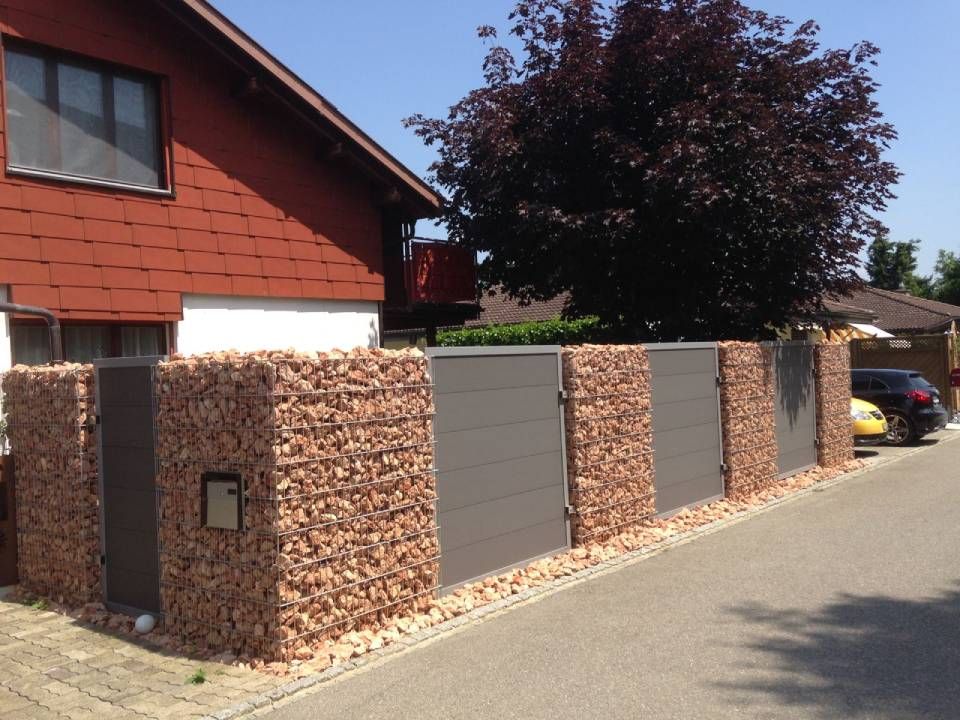 Modernes Haus mit einem steingrauen Sichtschutzzaun an einer Wohnstrasse, in der Nähe ein Baum und ein geparktes Auto.