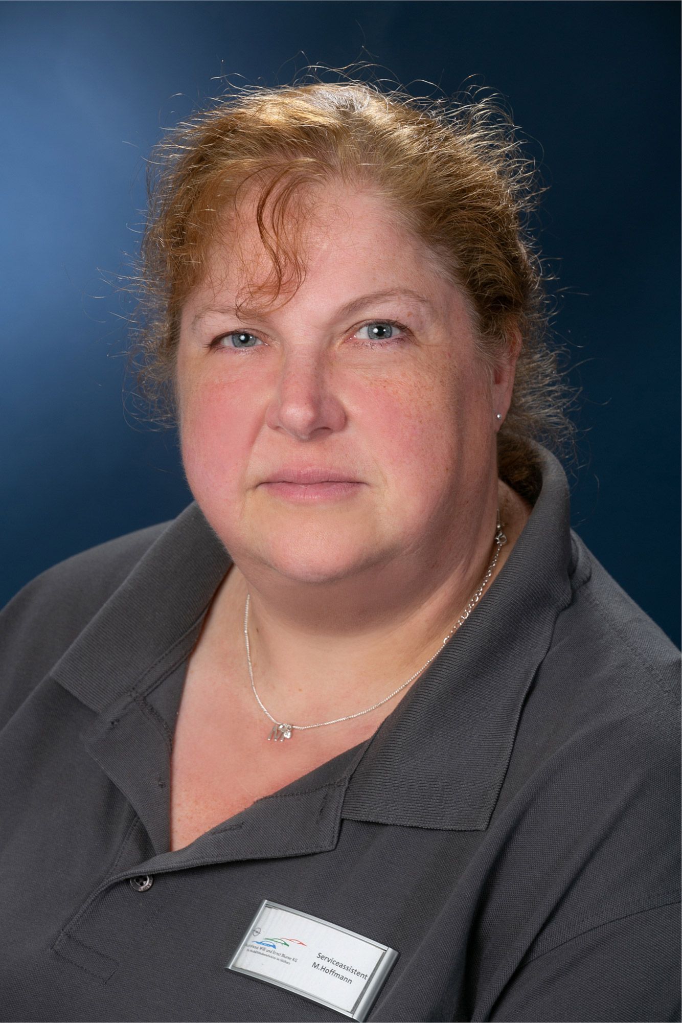 Eine Frau mit roten Haaren trägt ein graues Hemd und ein Namensschild.