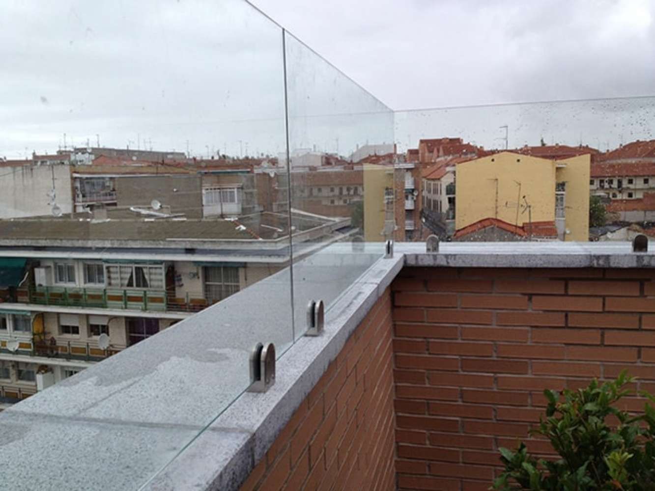 Un balcón con barandilla de cristal y vista a una ciudad.