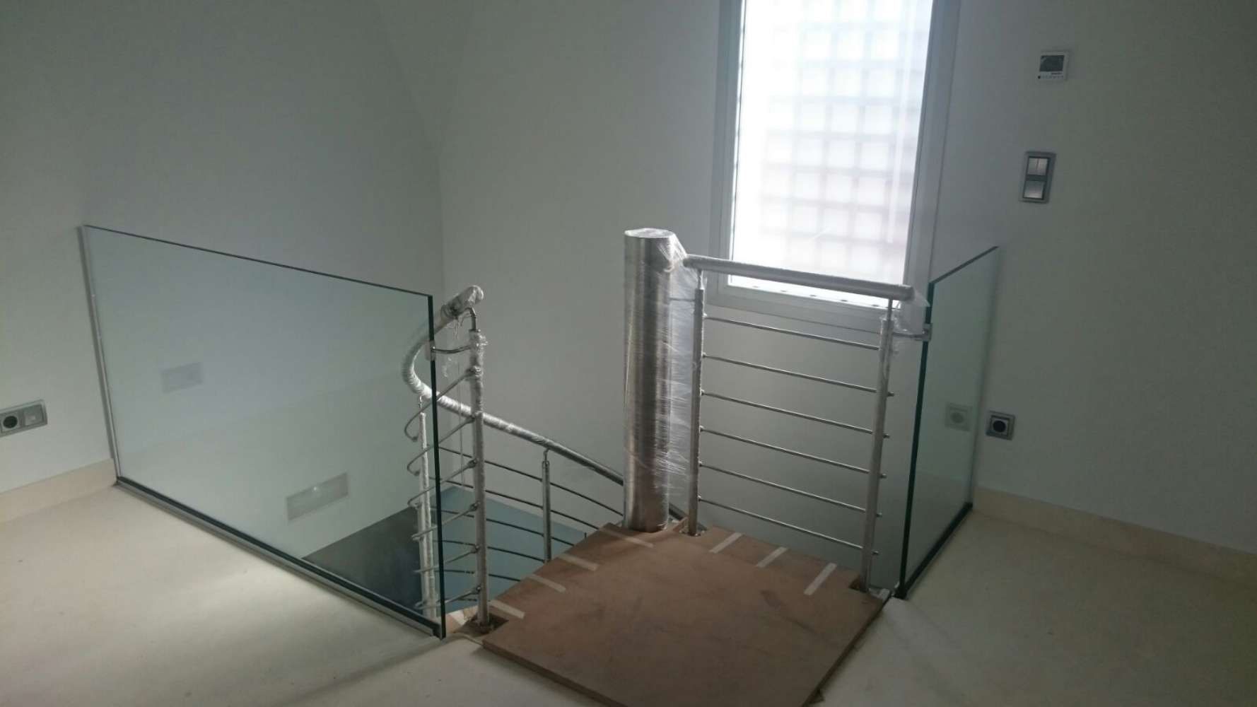 Una habitación vacía con una escalera de caracol y una barandilla de cristal.
