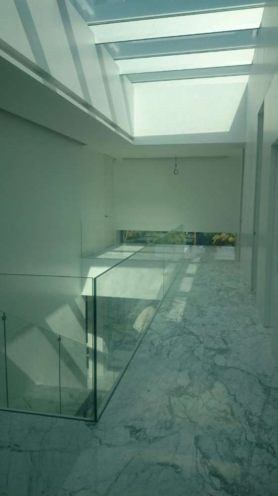 Un pasillo con barandilla de cristal y una claraboya en el techo.