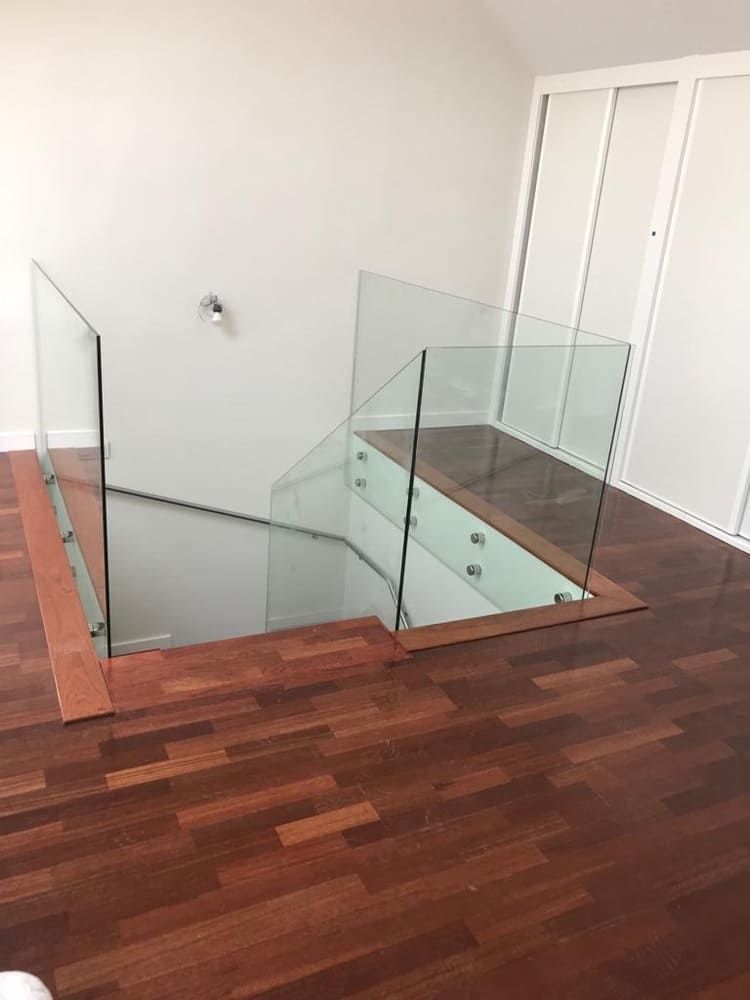 Una escalera con barandilla de cristal y suelo de madera.