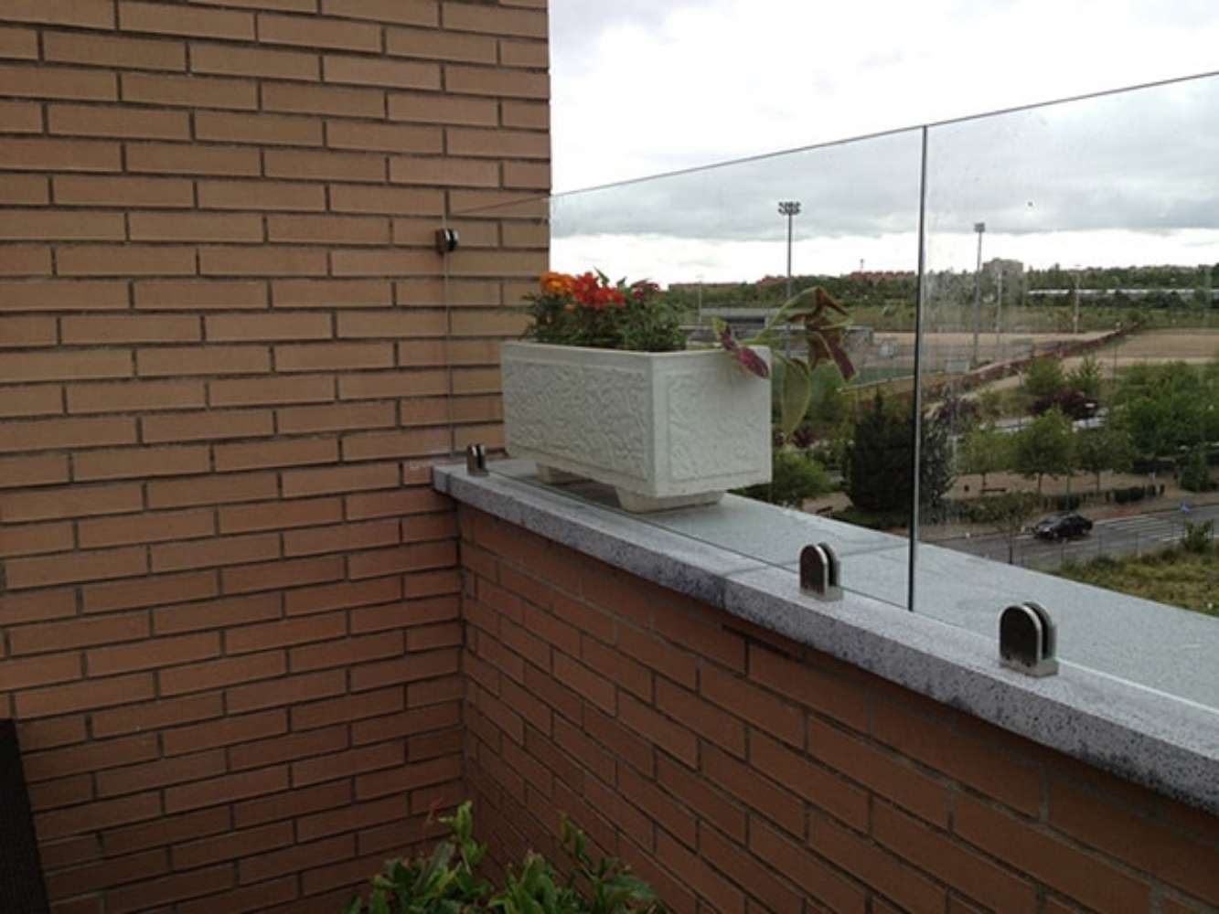 Un balcón con barandilla de cristal y una planta en maceta.