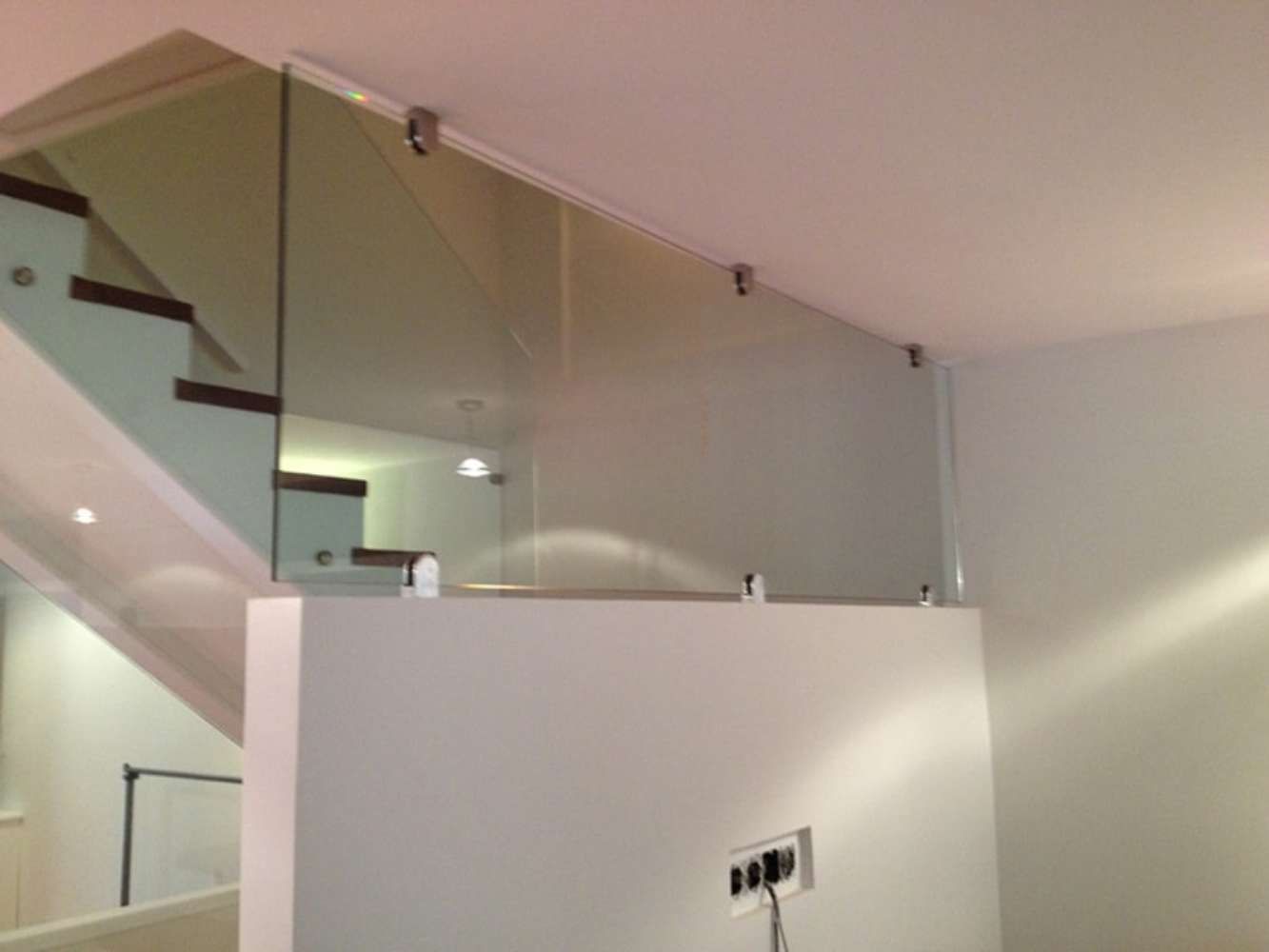 Una escalera con barandilla de cristal y una pared blanca.