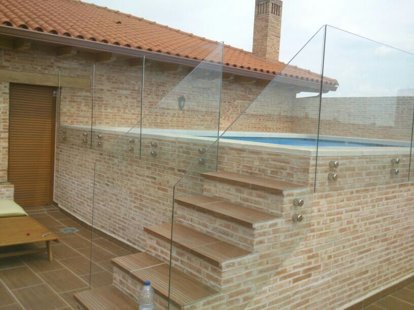 Escaleras que conducen a una piscina con barandilla de cristal.