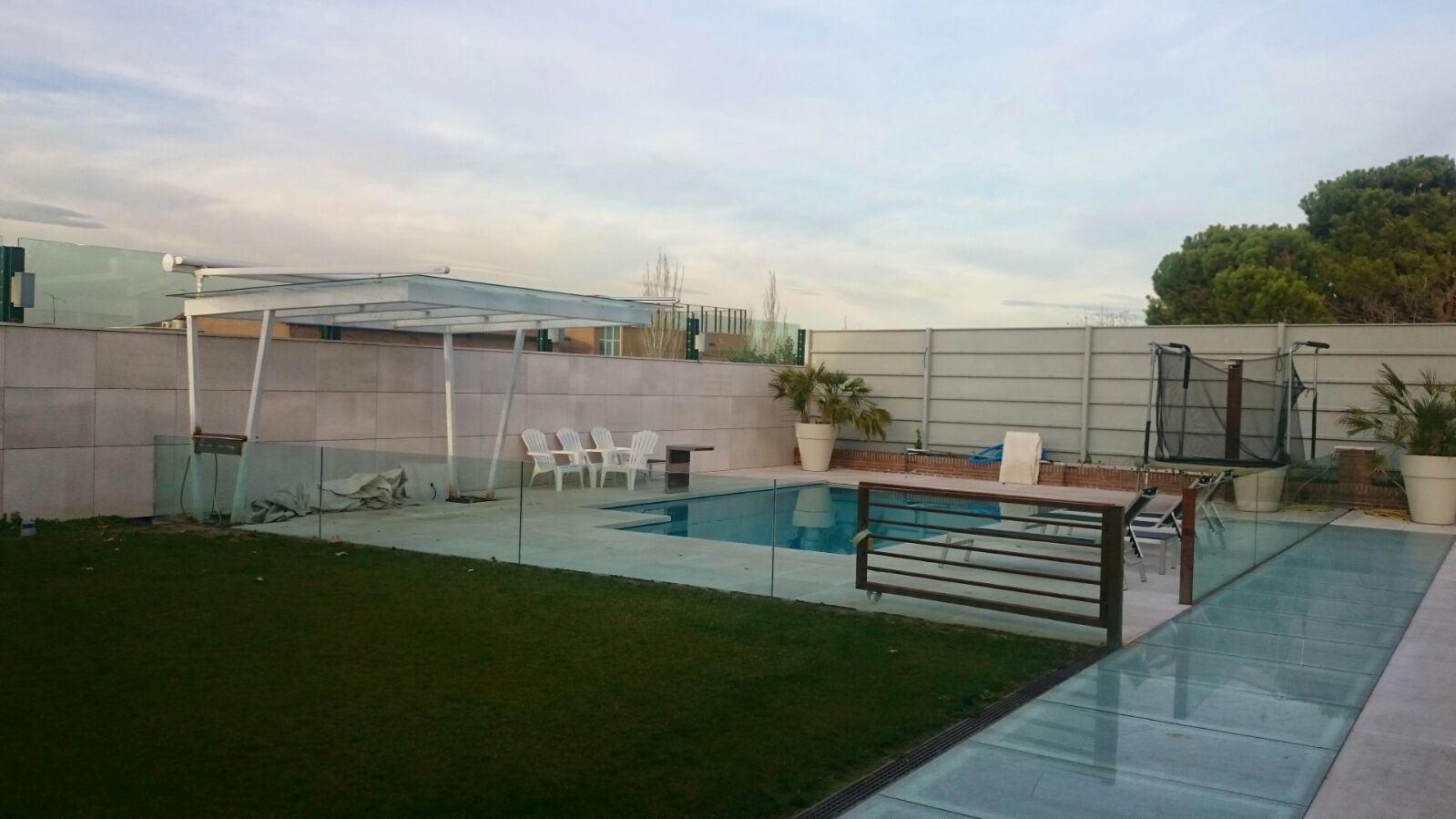 Una gran piscina está rodeada por una valla de cristal en un patio trasero.