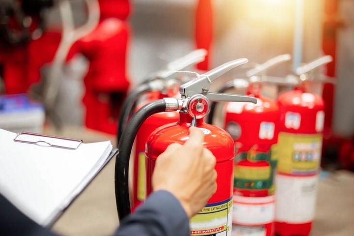 Una persona con una chaqueta azul revisa un extintor de incendios, sosteniendo un portapapeles
