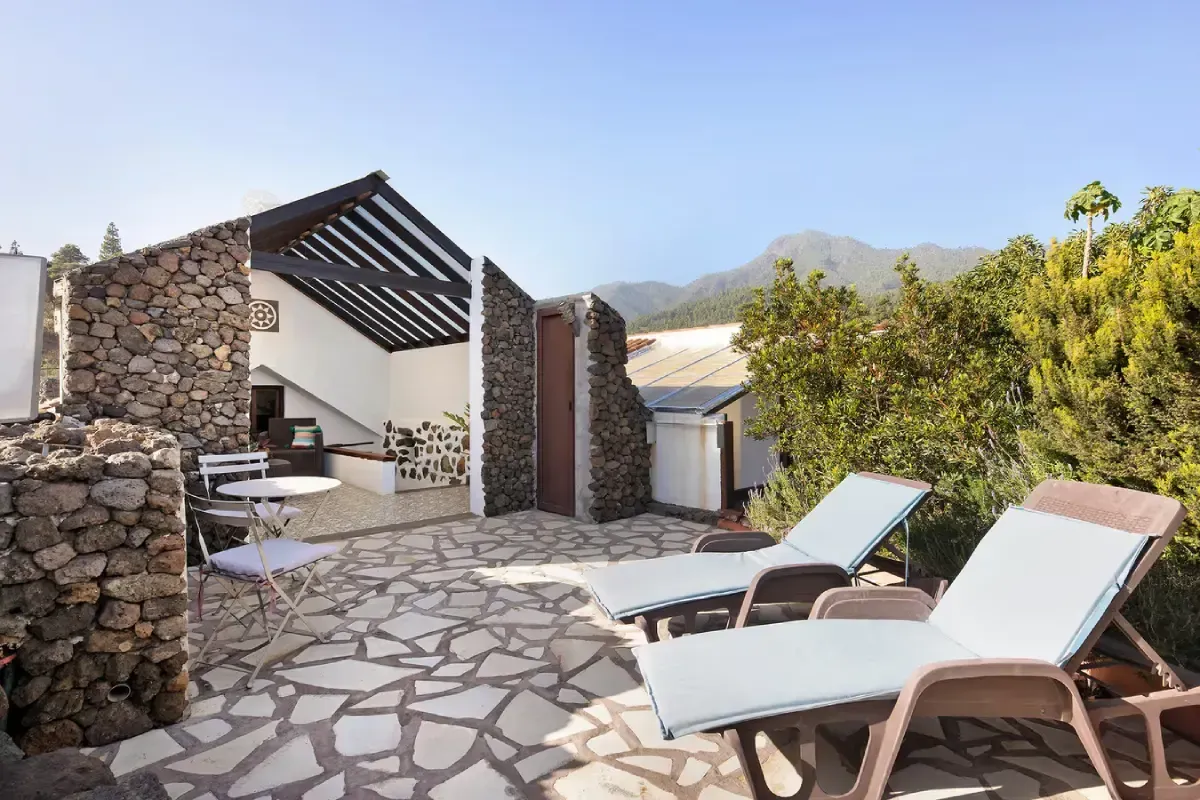 Patio con paredes de piedra, tumbonas y vista a la montaña en un día soleado.