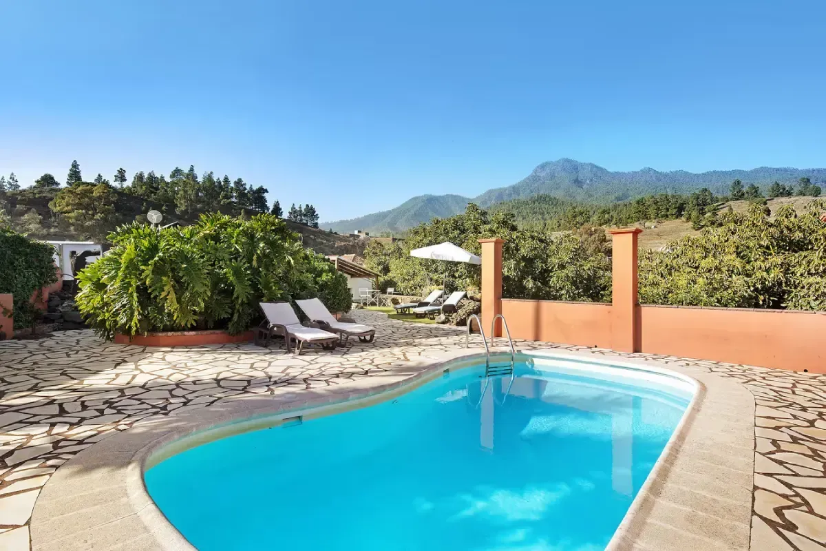 Piscina con tumbonas con vistas a una cordillera en un día soleado.