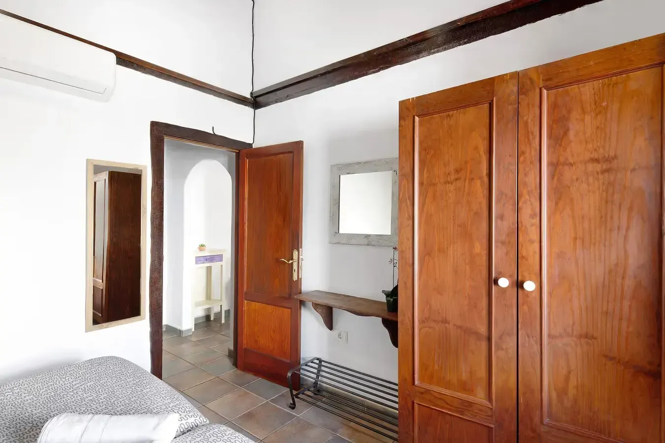 Interior de dormitorio con armario de madera, puerta abierta al baño, espejo y unidad de aire acondicionado.