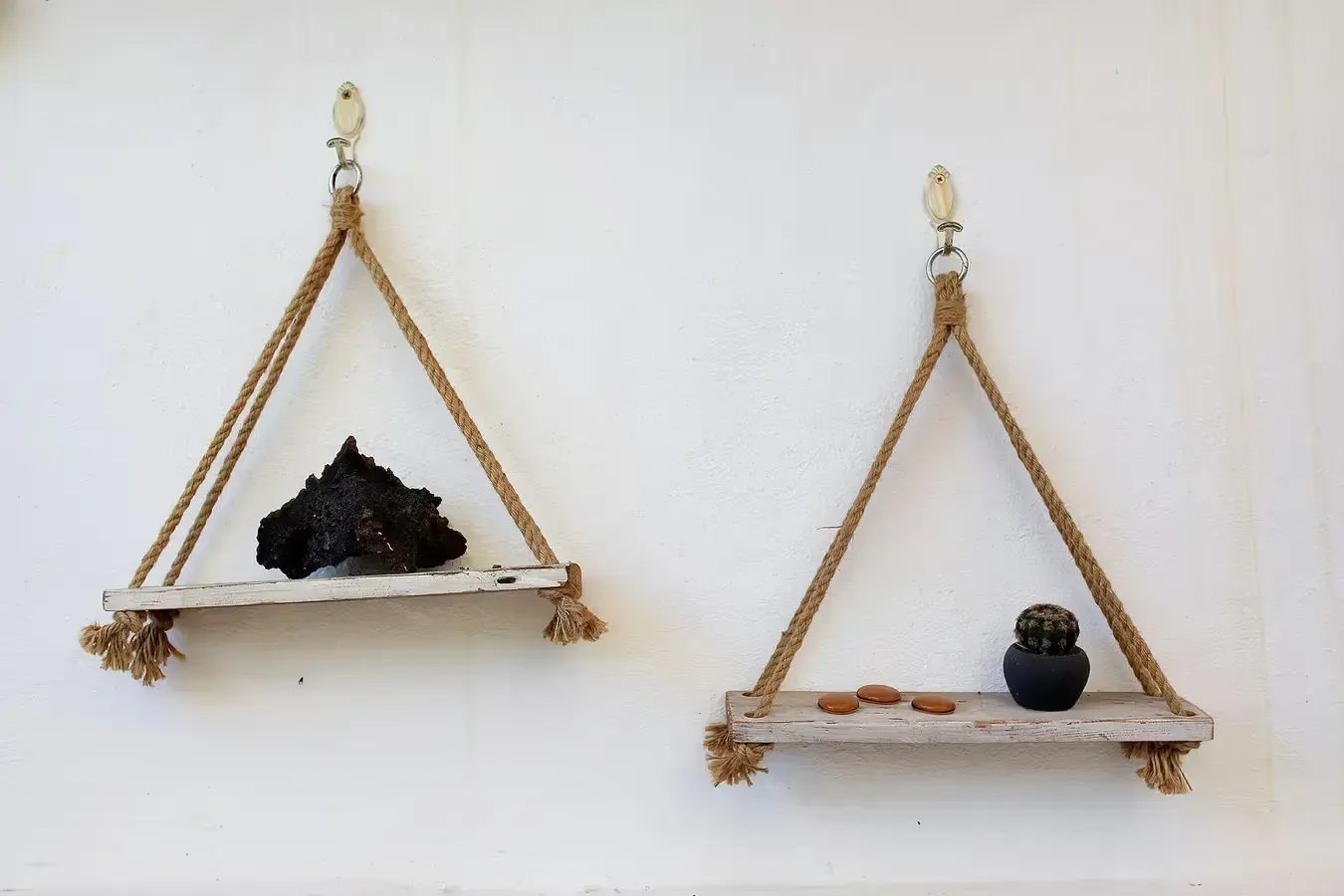 Dos estantes triangulares de madera colgados en una pared blanca, cada uno conteniendo objetos.