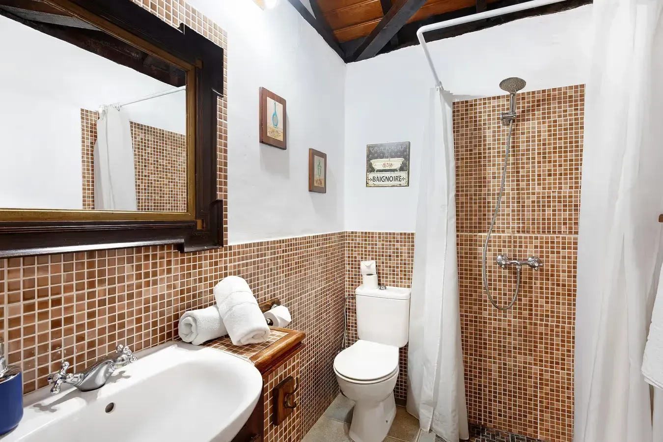 Baño con paredes de mosaico marrón, lavabo blanco, inodoro y ducha con cortina.