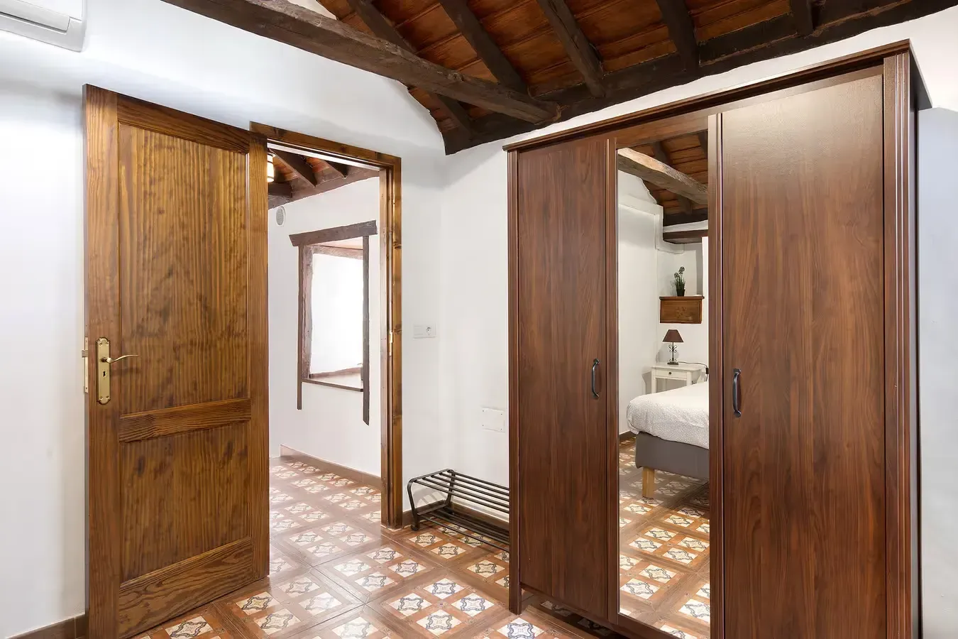 Dormitorio con puerta de madera, armario y suelo estampado. Vista a una habitación soleada con cama.