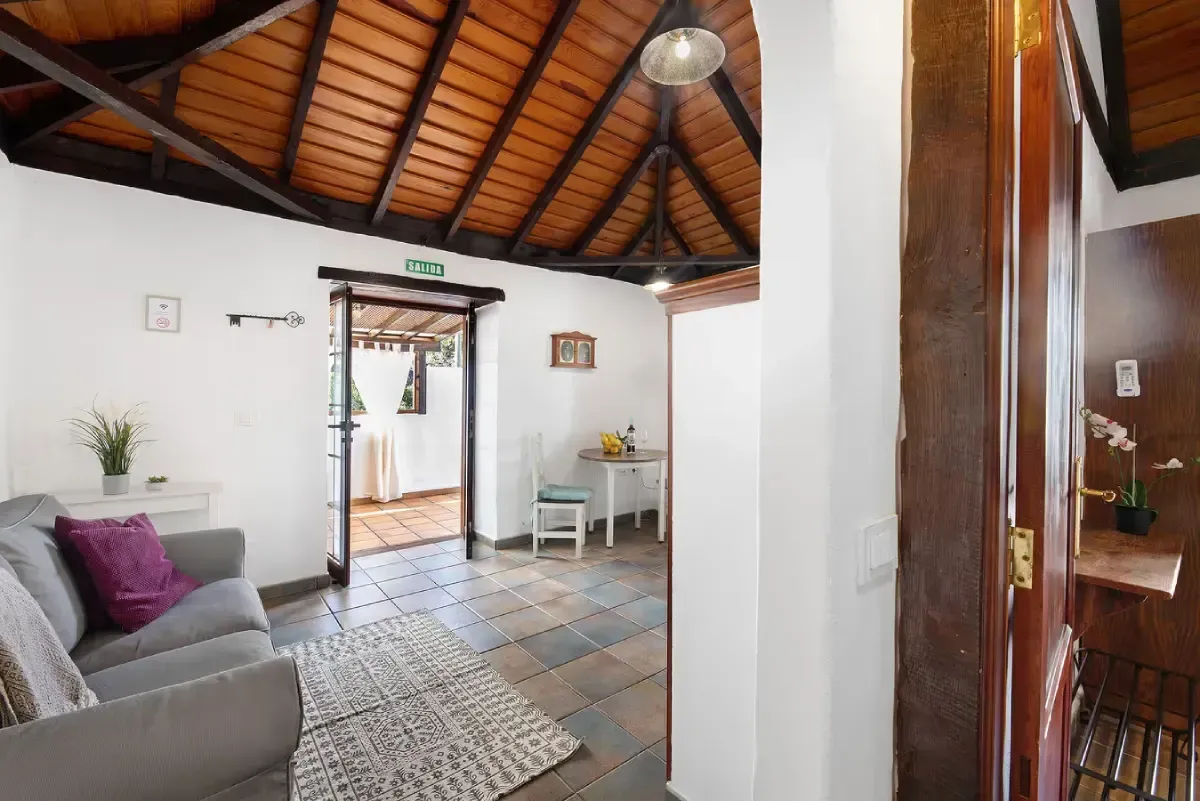 Sala de estar con sofá gris, techo de madera y puerta de entrada a otra habitación.