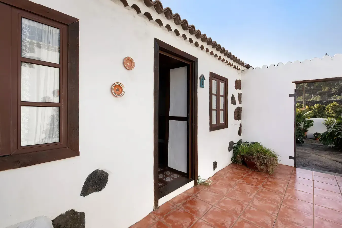 Edificio de estuco blanco con molduras marrones, patio con azulejos de terracota y puerta abierta.