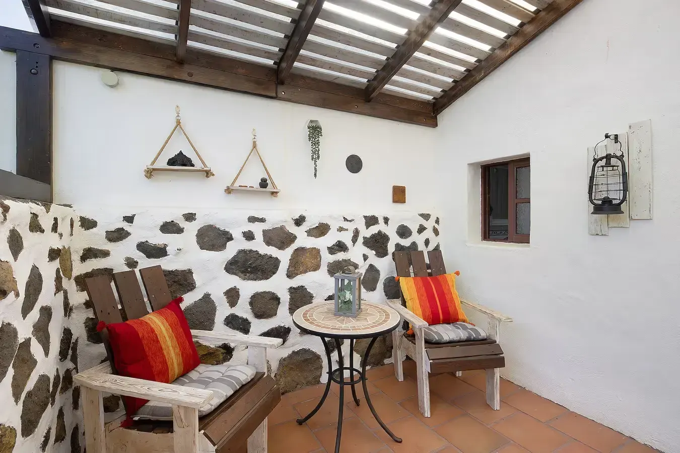 Patio con dos sillas, muro de piedra, mesa pequeña y elementos decorativos.