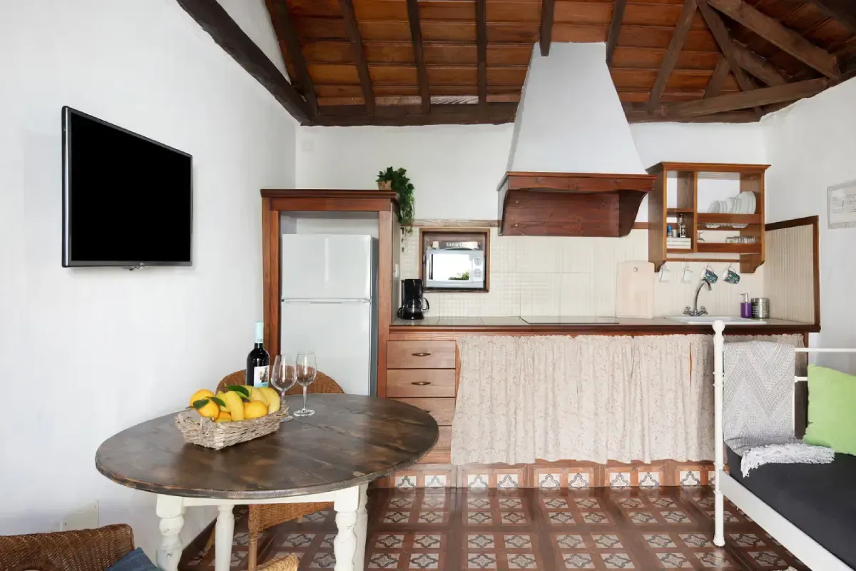 Acogedora cocina y comedor con mesa redonda de madera, limones, nevera y TV de pared.