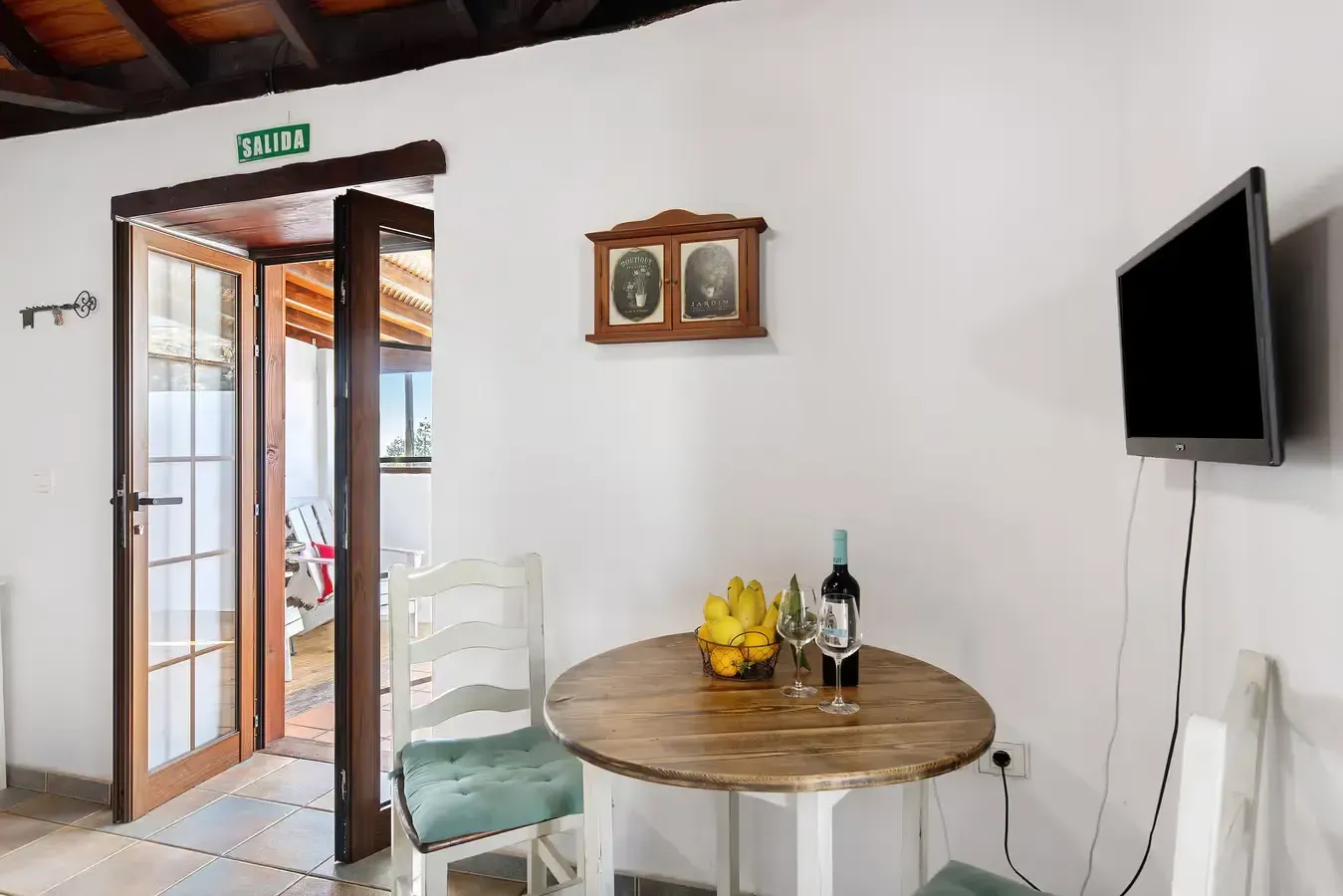 Interior con mesa redonda, sillas, TV y puertas abiertas a un patio.