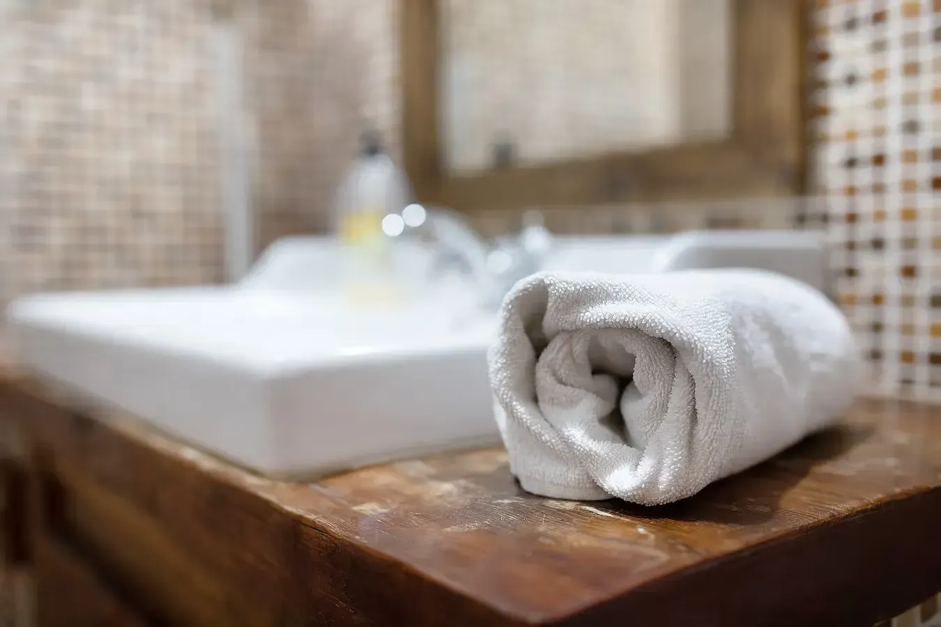 Toalla blanca enrollada sobre un mostrador de madera junto a un lavabo blanco en un baño.