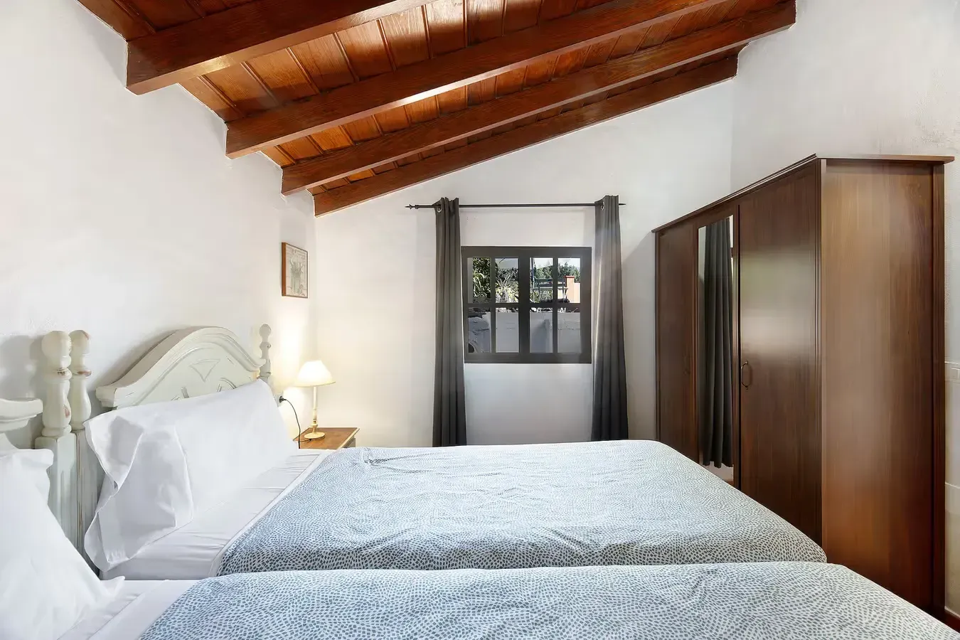 Dormitorio con dos camas individuales, vigas de madera, ventana y armario.