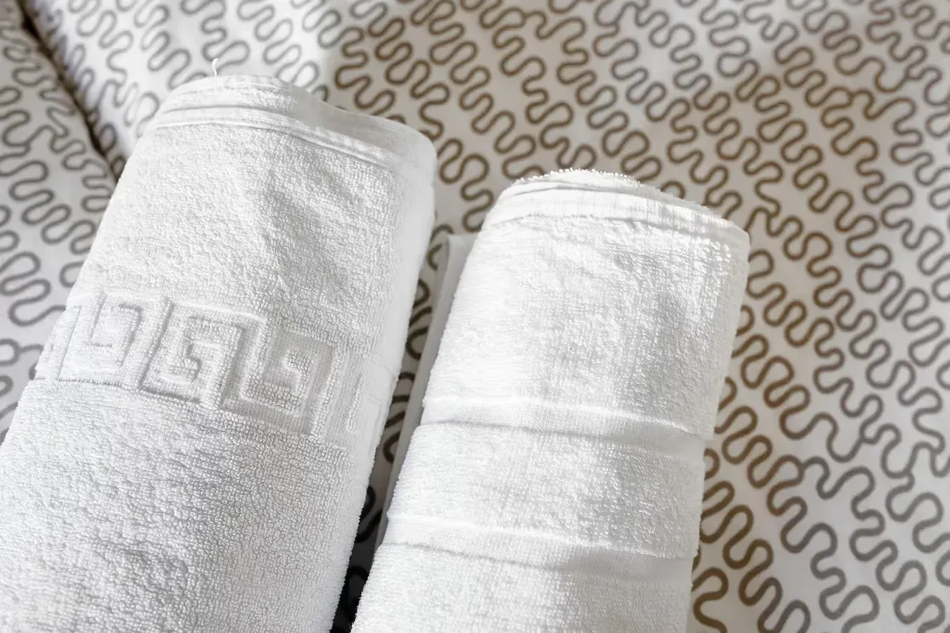 Dos toallas blancas enrolladas sobre una colcha estampada.