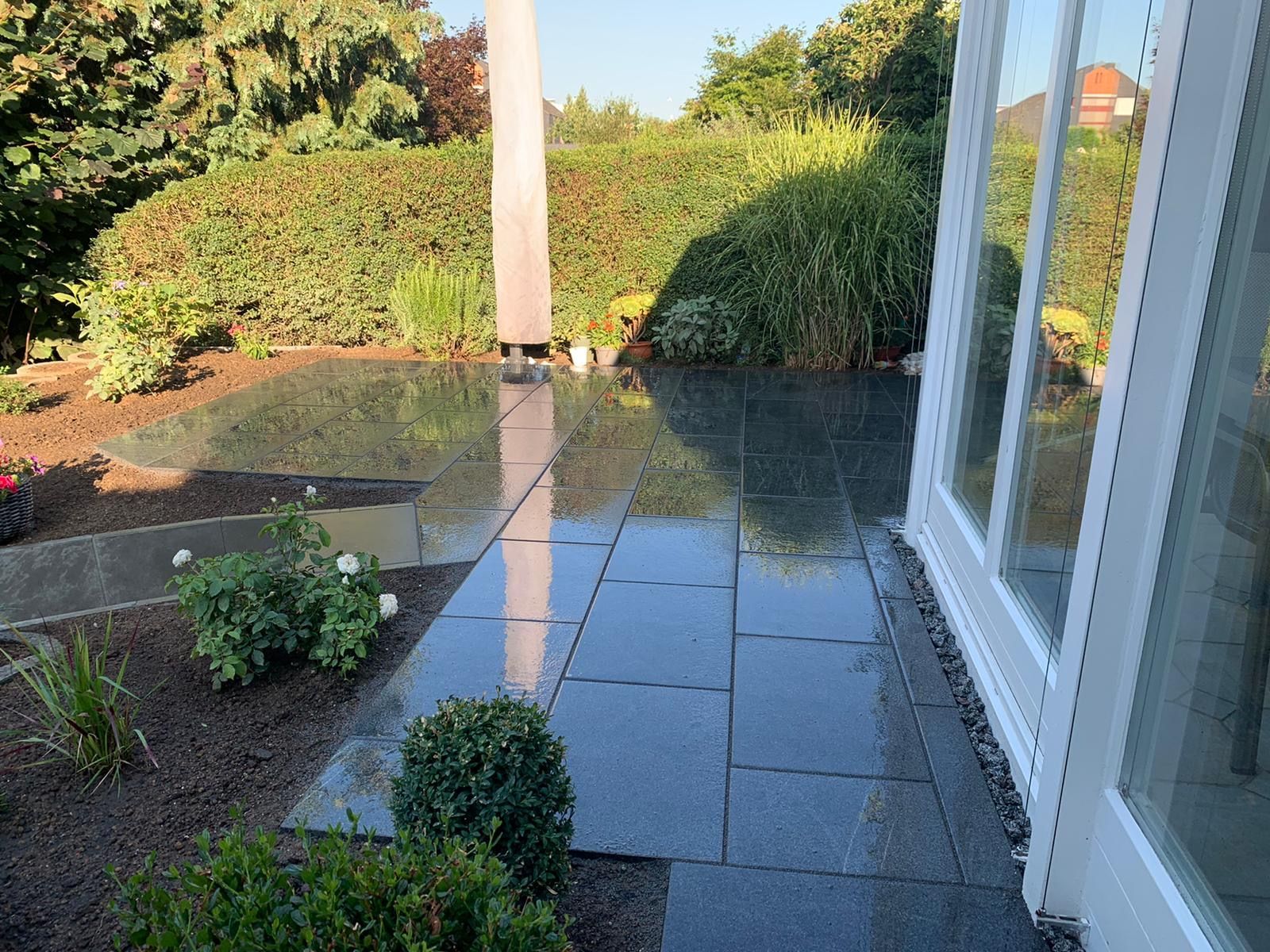 Spiegelnde, dunkle Terrassenplatten im Gartenbereich.