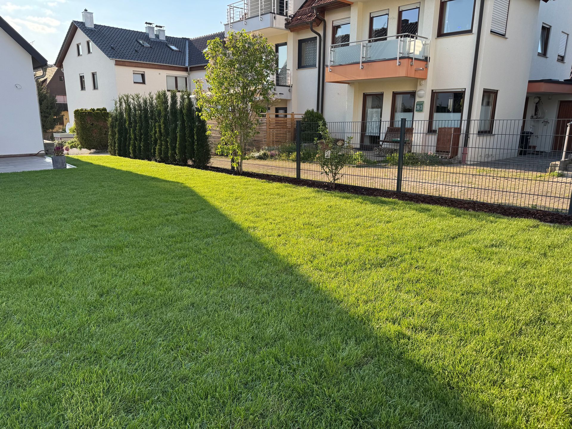 Gartenansicht mit Rasen, Zaun und angrenzenden Wohnhäusern.