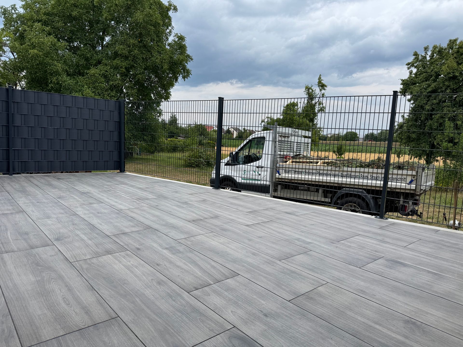 Moderne Terrasse mit dunkler Umzäunung und Blick auf Fuhrpark.