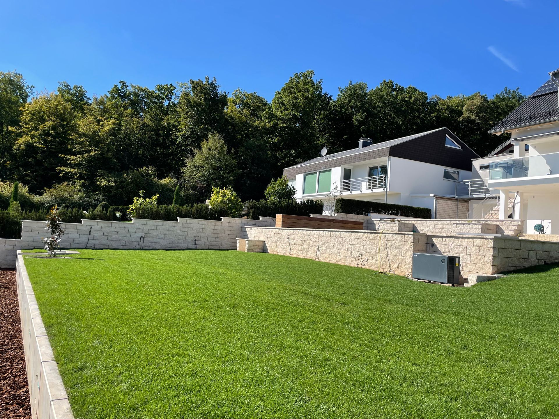 Gepflegter Rasen mit Natursteinmauer und moderner Terrasse.