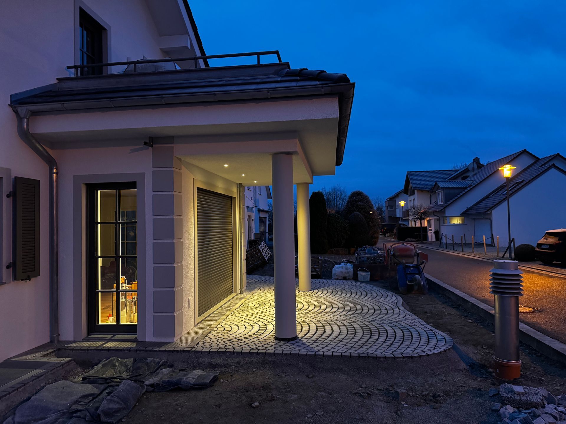 Beleuchteter Hauseingang mit Natursteinpflaster bei Nacht.