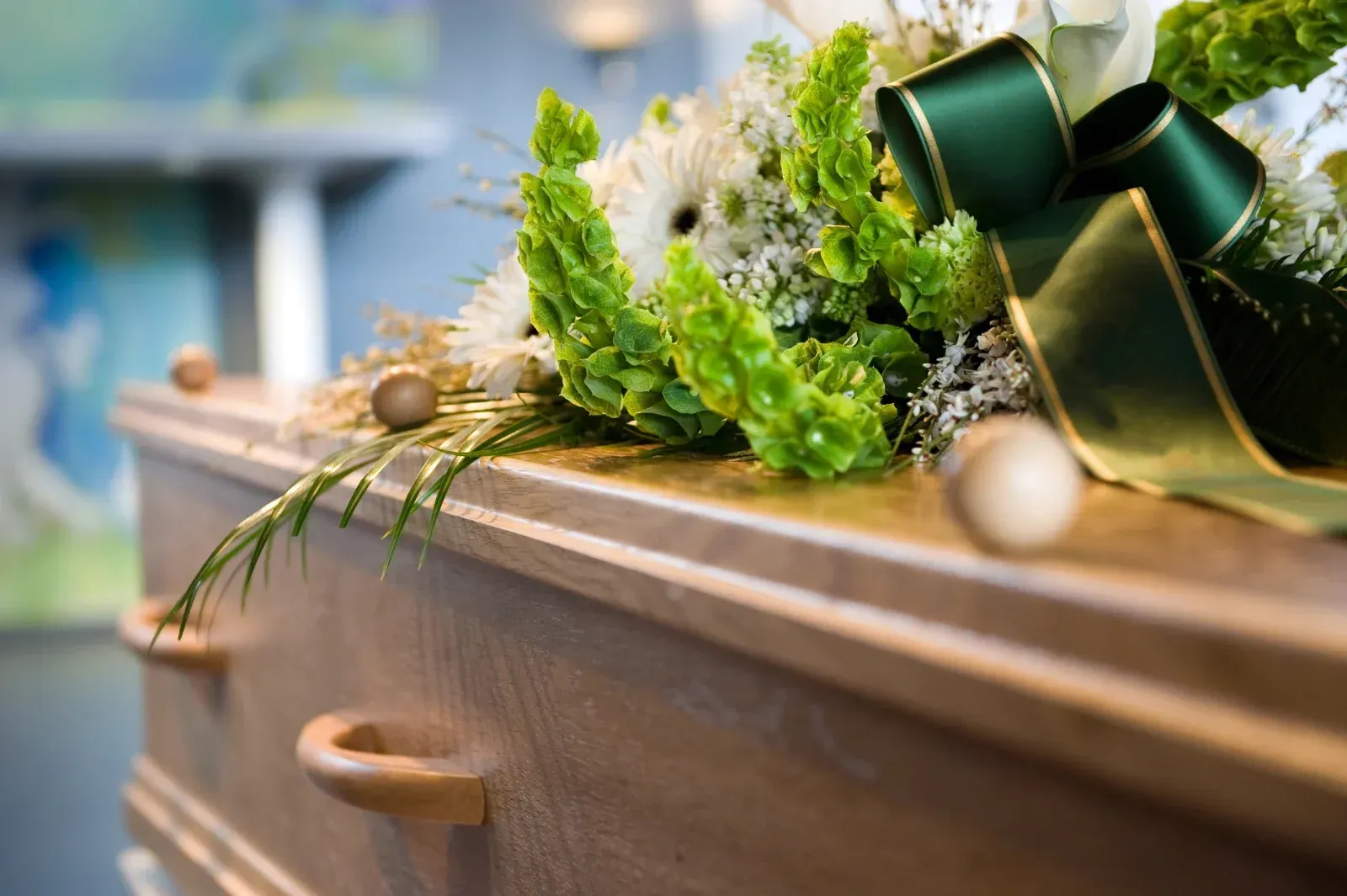 Holzschatulle mit Blumenarrangement, grünem Band und unscharfem Hintergrund.