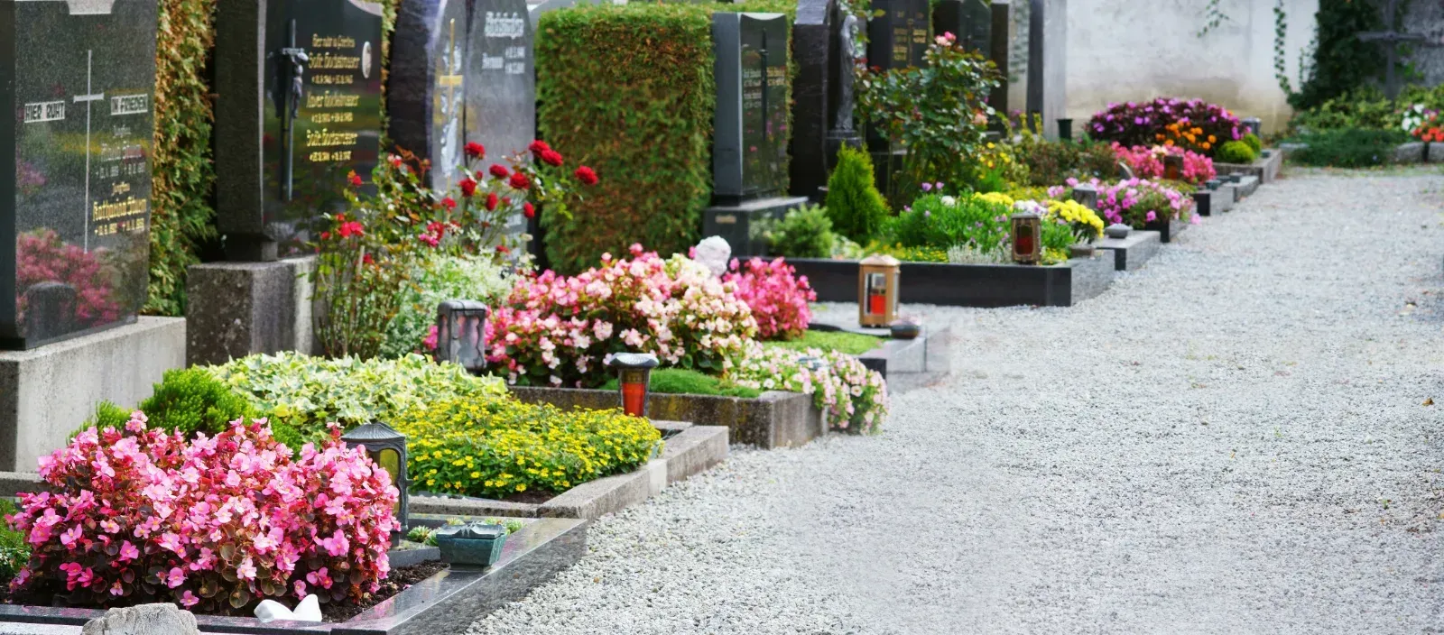 Reihen verzierter Grabsteine auf einem Friedhof mit blühenden Blumen und Kieswegen.