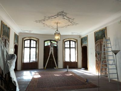 Eine Person auf einer Leiter malt kunstvolle Deckendetails in einem Raum mit großen Fenstern, a