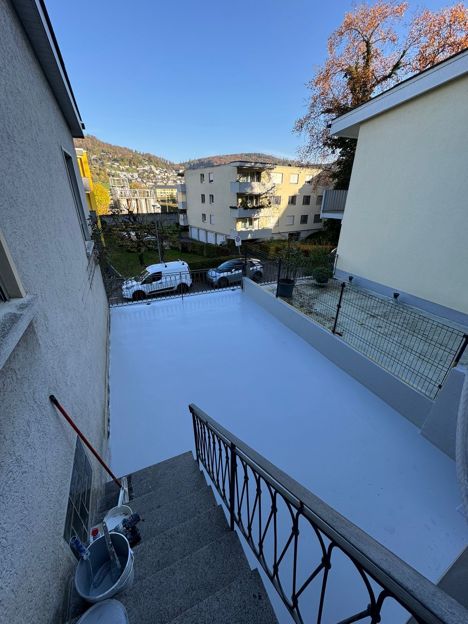 Außenansicht einer frisch gestrichenen grauen Terrasse. Im Hintergrund Gebäude und Bäume unter blauem Himmel.