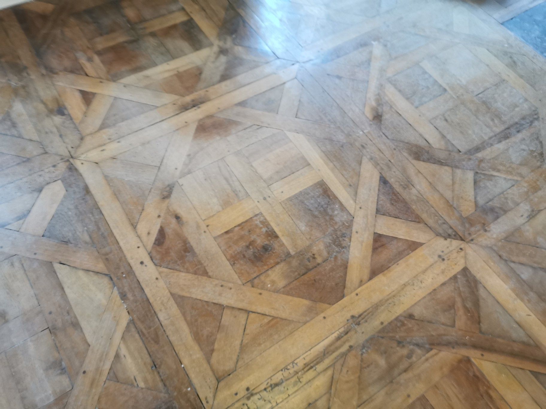 Un parquet en bois dur vieilli, orné d'un motif géométrique complexe en treillis composé de lattes de bois brun clair.