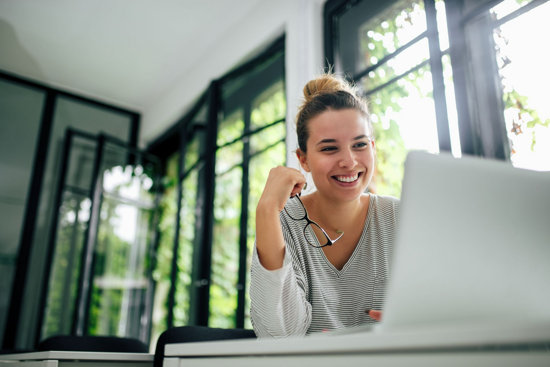 Une femme qui a ses lunettes dans les mains et sourit.