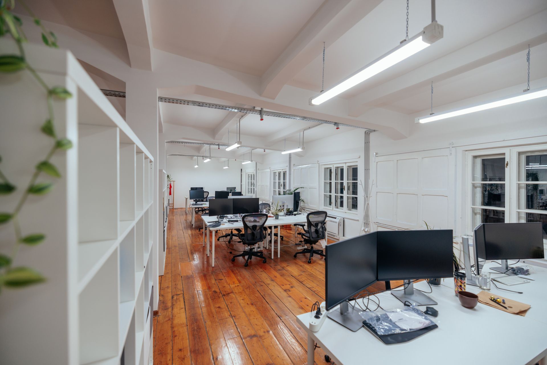 Un espace de bureau moderne et lumineux avec des bureaux blancs, des écrans d'ordinateur et des chaises sur un parquet ciré.